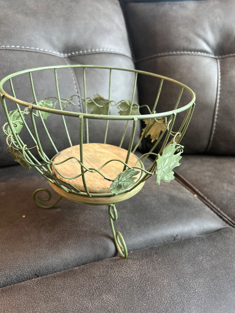 Green metal wire basket features decorative ivy leaves and a wooden base.